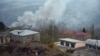 A truck loaded with firewood and other items is seen on a road in the town of Lachin (Berdzor) as smoke rises from a house set on fire by departing residents on November 30.