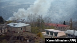 A truck loaded with firewood and other items is seen on a road in the town of Lachin (Berdzor) as smoke rises from a house set on fire by departing residents on November 30.