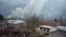 A truck loaded with firewood and other items is seen on a road in the town of Lachin (Berdzor) as smoke rises from a house set on fire by departing residents on November 30.