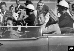 Presidenti John F.Kennedy duke përshëndetur qytetarët nga vetura e tij, pothuajse një minutë para se të qëllohej për vdekje më 22 nëntor 1963.