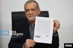 Iranian President Masud Pezeshkian holds up the signed memorandum of understanding with the United States on June 18.