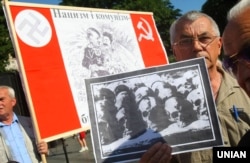 Учасник мітингу-реквієму тримає фото черепів та тлі плаката із зображенням Сталіна та Гітлера в день пам’яті жертв комуністичного і нацистського режимів. Львів, 22 червня 2011 року