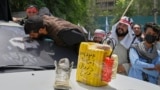 Egy férfi lehel csókot az afgán belügyminiszter, Sirajuddin Haqqani fotójára, amelyet egy autó szélvédőjére rögzítettek. A motorháztetőn az öngyilkos merényletek szimbóluma, egy sárga benzintartály és egy, a tálibok által hordott sportcipő a tálib hatalomátvétel 4. évfordulóján Kabulban augusztus 15-én