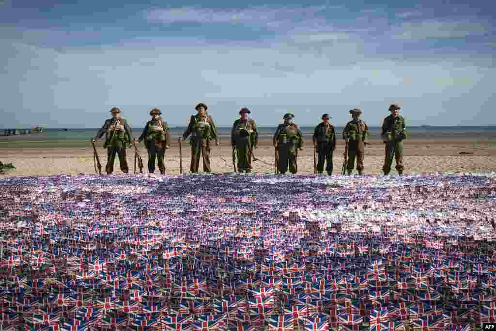 People wearing World War II-era British uniforms stand in front of British flags in Asnelles.