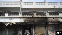 Pakistani police investigate the site of a burned market in a violence-hit western neighborhood of Karachi of July 8.