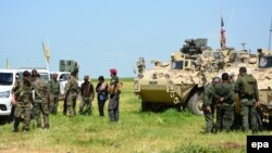 در این عکس از دو هفته پیش نیروهای «یگان‌های مدافع خلق» در کنار خودروی زرهی ارتش آمریکا در نزدیک مرز ترکیه دیده می‌شوند
