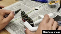 Një grua në një punëtori në Lviv duke ngjitur me shirit bateritë e cigareve elektronike të dërguara nga Leeds në një bllok që do të vendoset në një powerbank.