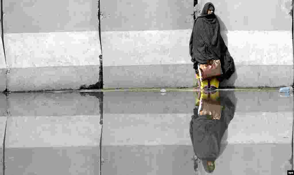 A Pakistani woman is reflected in a puddle of water as she waits to cross an inundated road in Islamabad on June 23. (epa/T. Mughal)