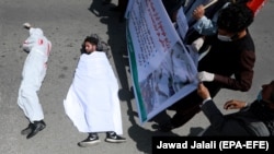 Afghan men wearing clothes spattered in blood lay down on a road as protesters shout slogans against the Iranian regime and demand justice during a protest outside the Iranian Embassy in Kabul on May 7.