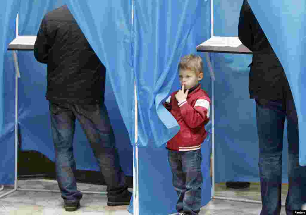 A boy peers from behind a curtain at a polling station in Kyiv.