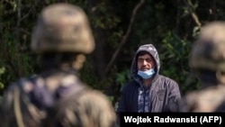 Польские пограничники стоят рядом с мигрантом, предположительно из Афганистана, в небольшой деревне на северо-востоке Польши, недалеко от границы с Беларусью, 20 августа 2021 года