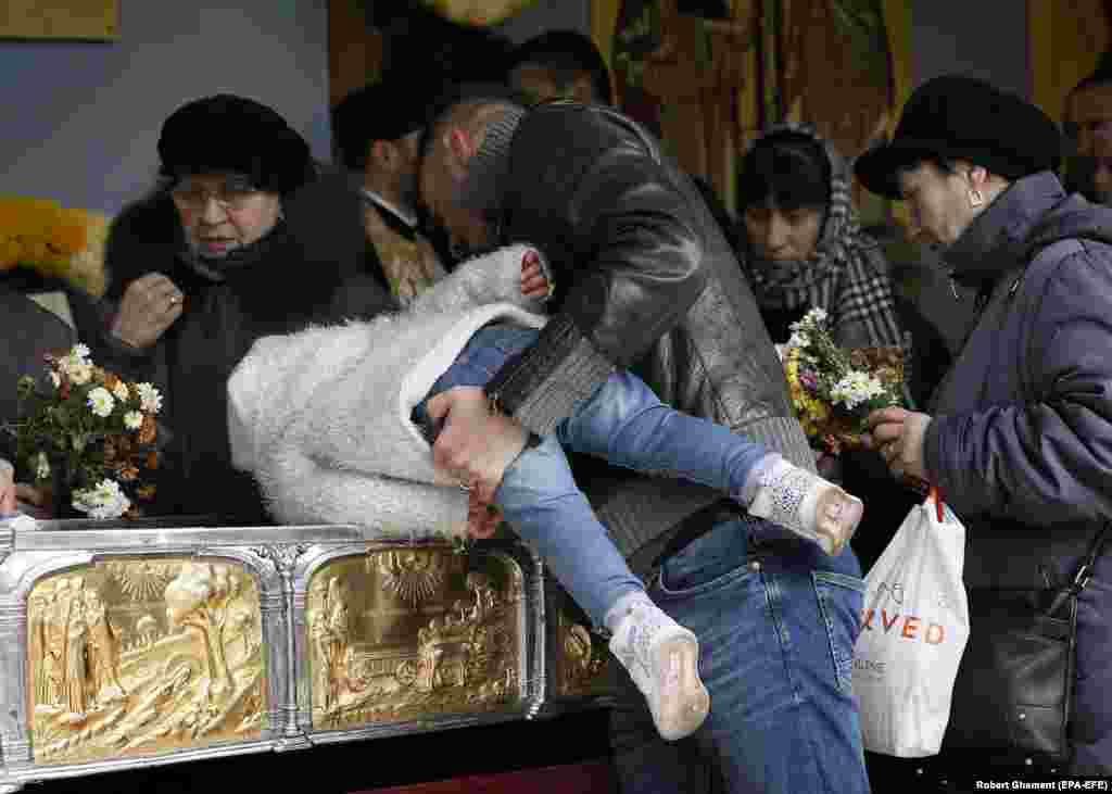 A Romanian father helps his boy to kiss the golden box containing the relics of Saint Dimitrie Basarabov during a Mass attended by Russian Orthodox Patriarch Kirill at the Patriarchal Cathedral in Bucharest. ( epa-EFE/Robert Ghement)