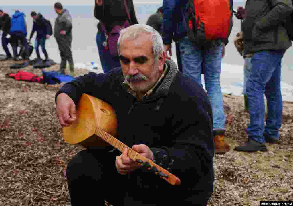 Nazmi Jolak, a Syrian Kurdish farmer, plays his saz after landing on the coast of Lesbos as the refugee boat he arrived on is dismantled behind him. The 52-year-old refugee from Aleppo carried the instrument,wrapped in plastic, across the sea. He is now hoping to join his son in Dortmund, Germany.