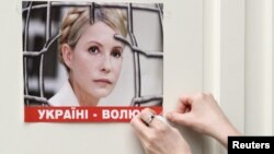 Юлия Тимошенко бейнеленген плакатты жапсырып жатқан адам. (Көрнекі сурет)