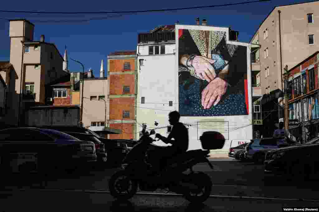 Një person me motoçikletë duke kaluar pranë një murali, në Ferizaj.