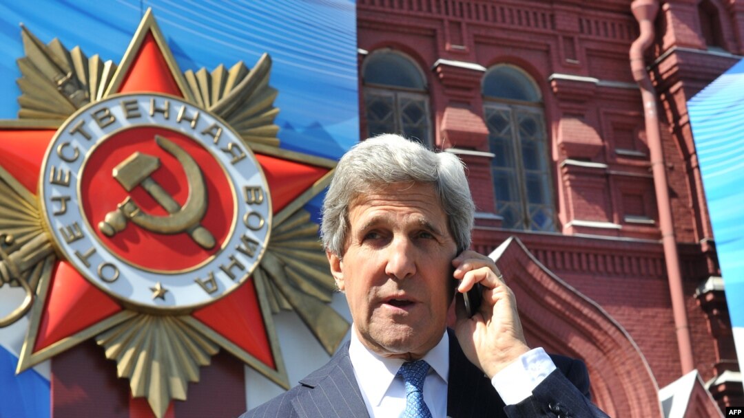 U.S. Secretary of State John Kerry talks on a cell phone as he walks on May 7 in front of a giant poster marking the upcoming Victory Day on the Red Square in Moscow.