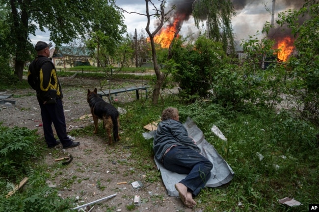 Një burrë shtrihet në tokë teksa e shikon shtëpinë e vet duke u djegur si pasojë e një sulmi rus ajror në Vovçanks, Ukrainë, 11 maj 2024.