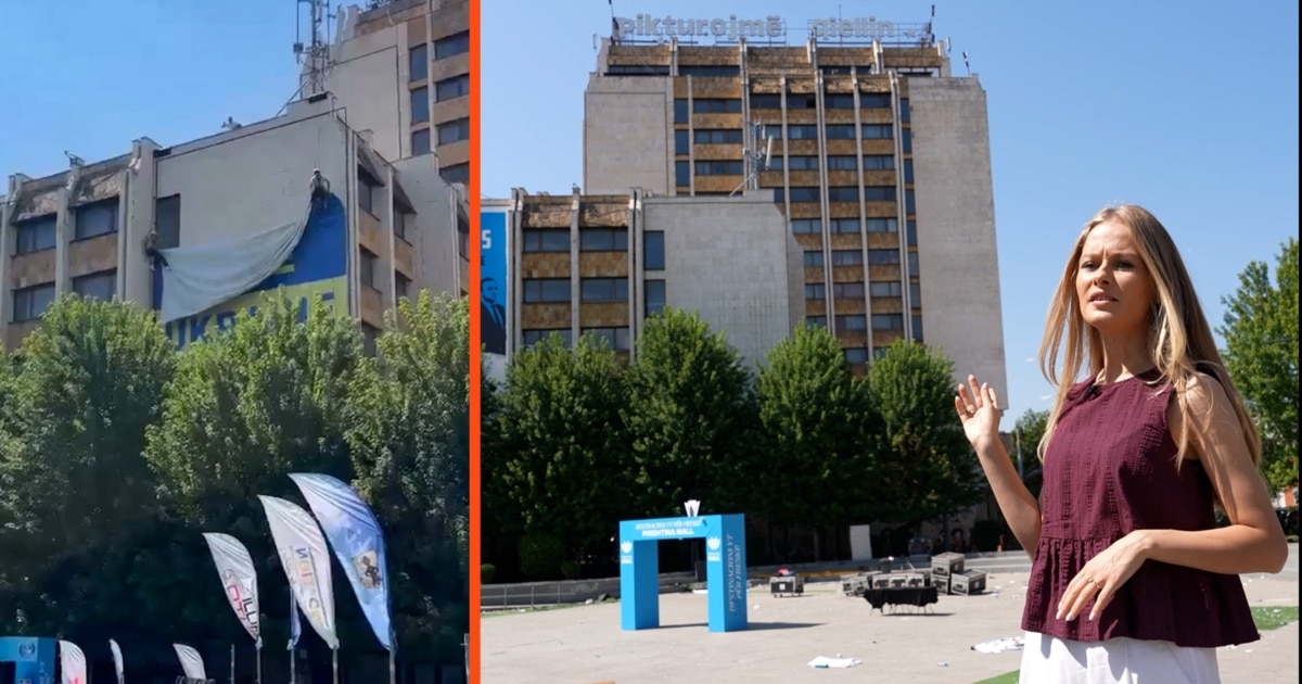 A woman stands outdoors in front of large buildings.
