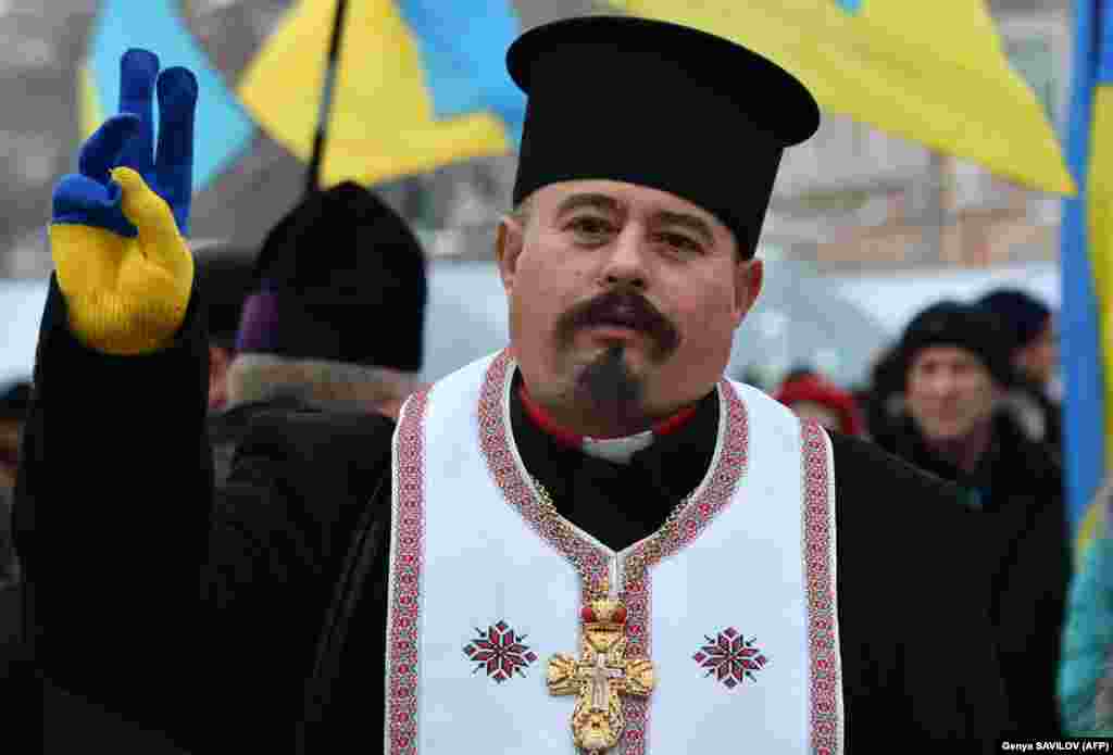 A priest flashes a V sign as he wears a Ukrainian-flag-colored glove as outside St. Sophia Cathedral in Kyiv on December 15 where Ukrainian Orthodox leaders agreed on the creation of a new national Orthodox Church and elected a leader to head it. (AFP/Genya Savilov)