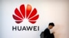 Un bărbat își folosește smartphone-ul în timp ce stă lângă un panou publicitar pentru firma chineză de tehnologie Huawei (ilustrație generică).