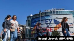Disa persona ecin pranë zyrës së BE-së ku janë vendosur disa logo ku shkruan “BE për ty”. Shkup, 18 tetor, 2019.
