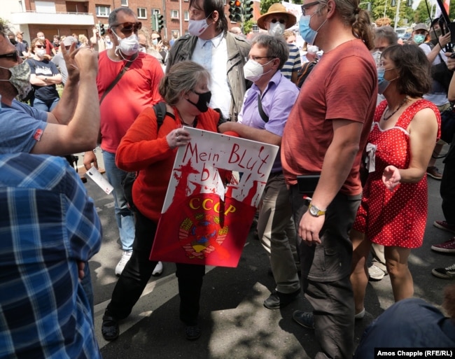 Yekaterina Maldon is jostled by members of the crowd. The sign says “My blood please” above the emblem of the Soviet Union.