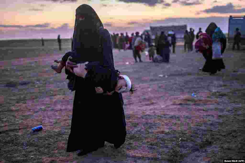 A woman carries her injured child as she walks to members of the Kurdish-led Syrian Democratic Forces (SDF) just after leaving the Islamic State group&#39;s last holdout of Baghouz in the eastern Syrian Deir Ezzor Province. (AFP/Bulent Kilic)