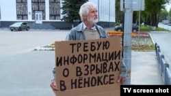In a video grab from Severodvinsk TV, a man stands outside the city administration building on August 13, holding a cardboard sign demanding information about the accident in Nyonoksa.