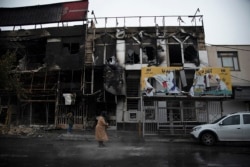 People walk past buildings which burned during protests that followed the authorities' decision to raise gasoline prices, in the city of Karaj, November 18, 2019