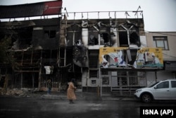 People walk past buildings which burned during protests that followed the authorities' decision to raise gasoline prices, in the city of Karaj, November 18, 2019