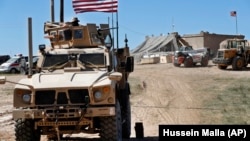 A U.S. soldier sits on an armored vehicle behind a sand barrier at a newly installed position near the front line between the U.S-backed Syrian Manbij Military Council and the Turkish-backed fighters, in Manbij, northern Syria.