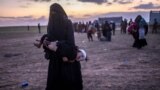 SYRIA -- A fully veiled woman carries her injured child as she walks to members of the Kurdish-led Syrian Democratic Forces (SDF) just after leaving the Islamic State group's last holdout of Baghouz, in the eastern Syrian Deir Ezzor province on March 4, 2