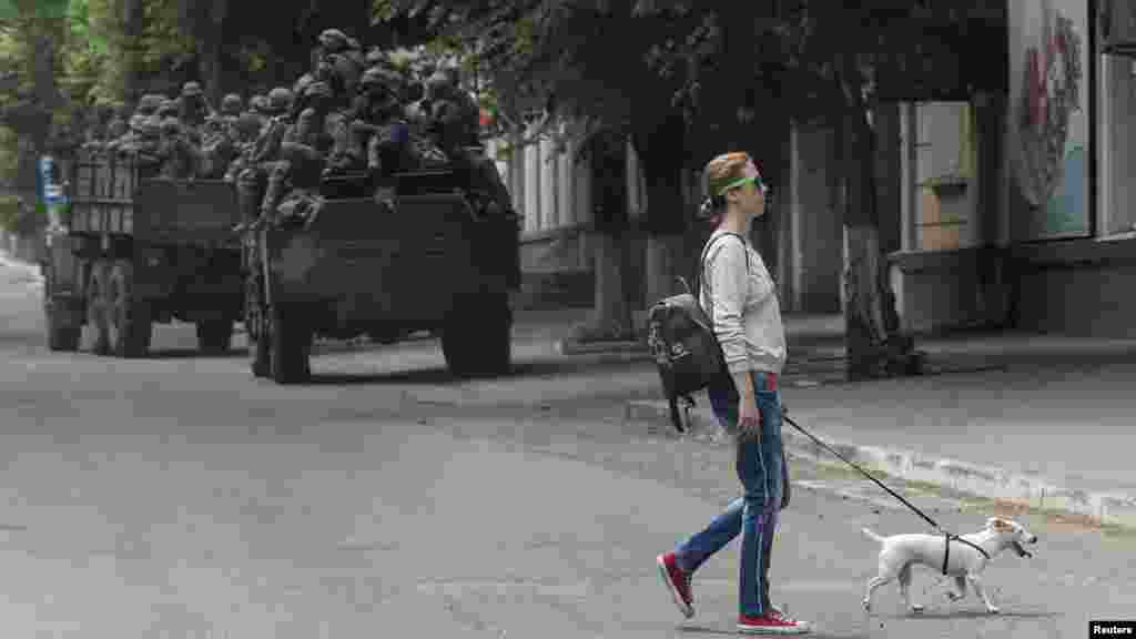 Женщина переходит улицу, в то время как украинская военная техника заезжает на позицию. Город Бахмут подвергся интенсивному артиллерийскому обстрелу со стороны российских войск.