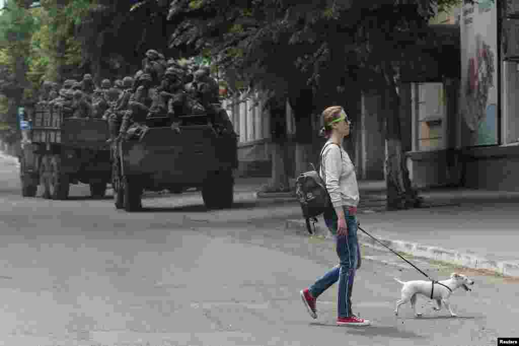 Egy helyi nő sétáltatja a kutyáját Bahmutban, a harci&nbsp; pozíciójukra vonuló ukrán katonai járművek mellett. Az orosz csapatok hevesen támadják a várost