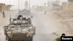 A convoy of Canadian armored vehicles passes an Afghan man on the main highway outside the village of Bazaar-e Panjway, in Afghanistan.