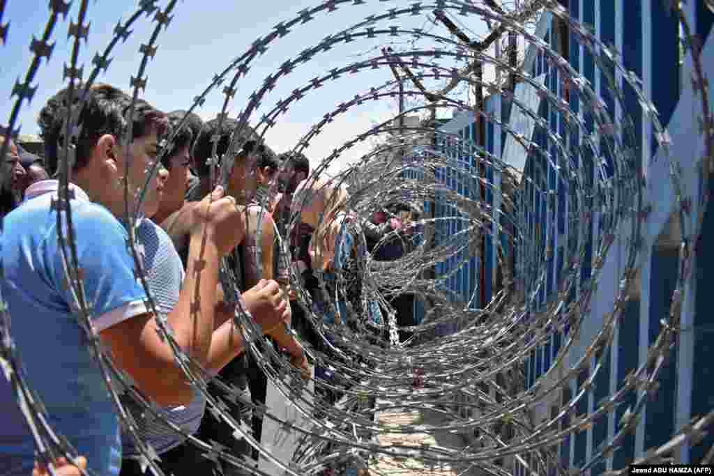 Youths from a camp for the displaced in the Syrian village of Al-Rafid clutch a barbed-wire fence near a checkpoint along the border with the Israeli-annexed Golan Heights during a protest against the Syrian government and calling for international protection. (AFP/Jawad Abu Hamza)