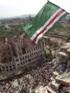 RUSSIA -- A Chechen man waves the national flag from the roof of the destroyed presidential palace 07 September 1995. 