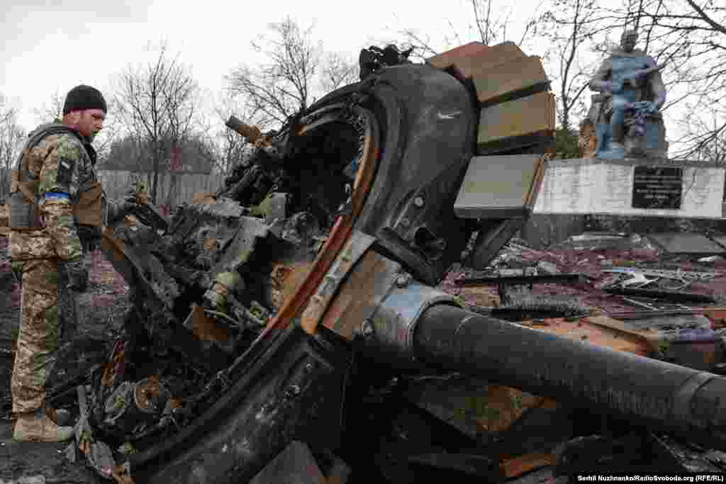 Український військовій 10-ї окремої гірсько-штурмової бригади «Едельвейс» оглядає знищений російський танк Т-72. Біля пошкодженого меморіалу загиблим воїнам у Другій світовій війні у нещодавно звільненому селі Лук’янівка на Київщині, 27 березня 2022 року