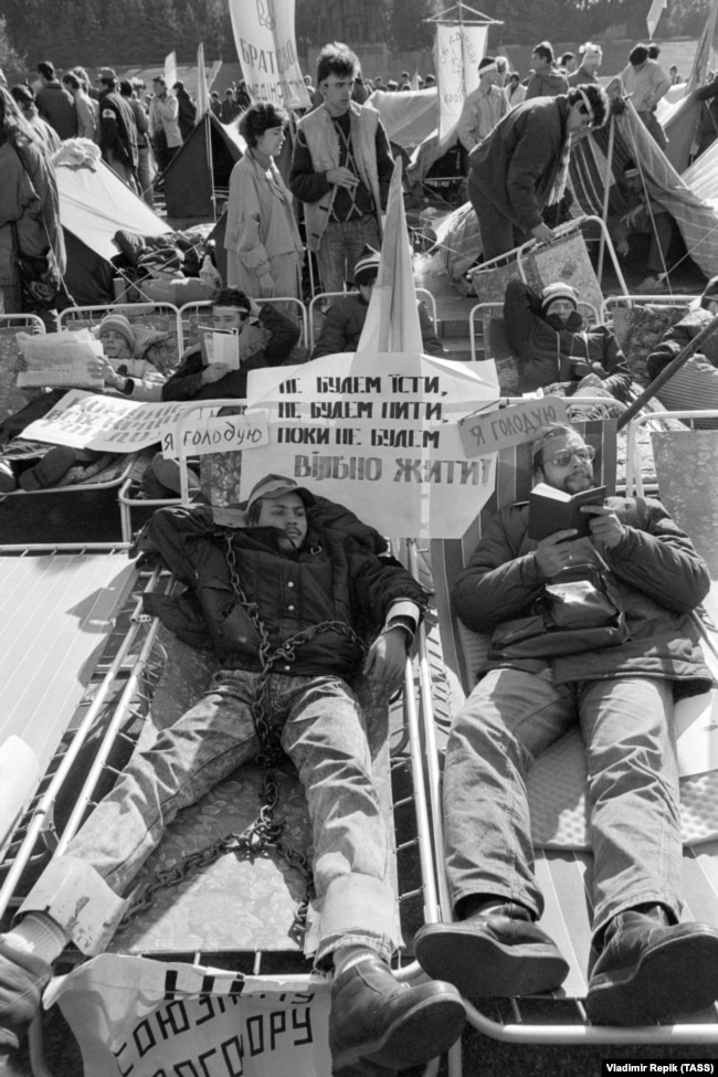A student hunger striker wearing symbolic shackles. The sign reads: “We won’t eat, we won’t drink until we will live freely."