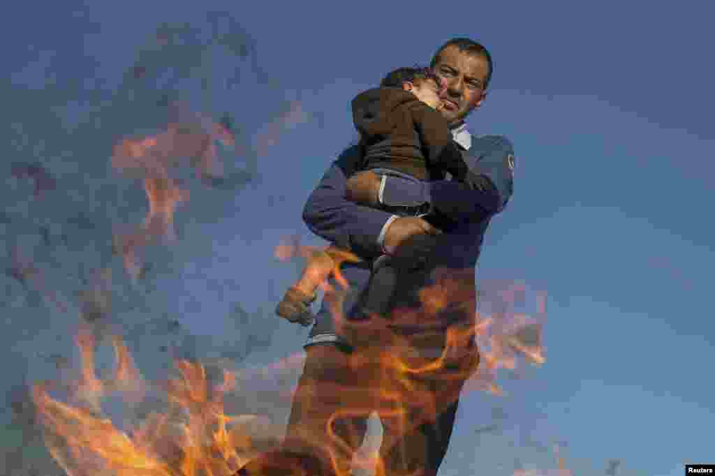 A migrant holds a child as they warm themselves by the fire in a makeshift camp at a collection point in the village of Roszke, Hungary. (Reuters/​Marko Djurica)