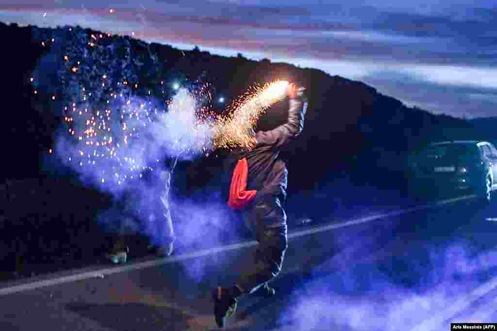 A man throws a flare at Greek riot police in clashes at a demonstration against the construction of a new migrant camp near the town of Mantamados on the northeastern Aegean island of Lesbos. (AFP/Aris Messinis)