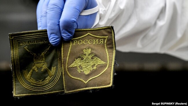 A Ukrainian forensic expert shows patches found on the body of a Russian soldier exhumed in the village of Zavalivka, west of Kyiv, on May 11.