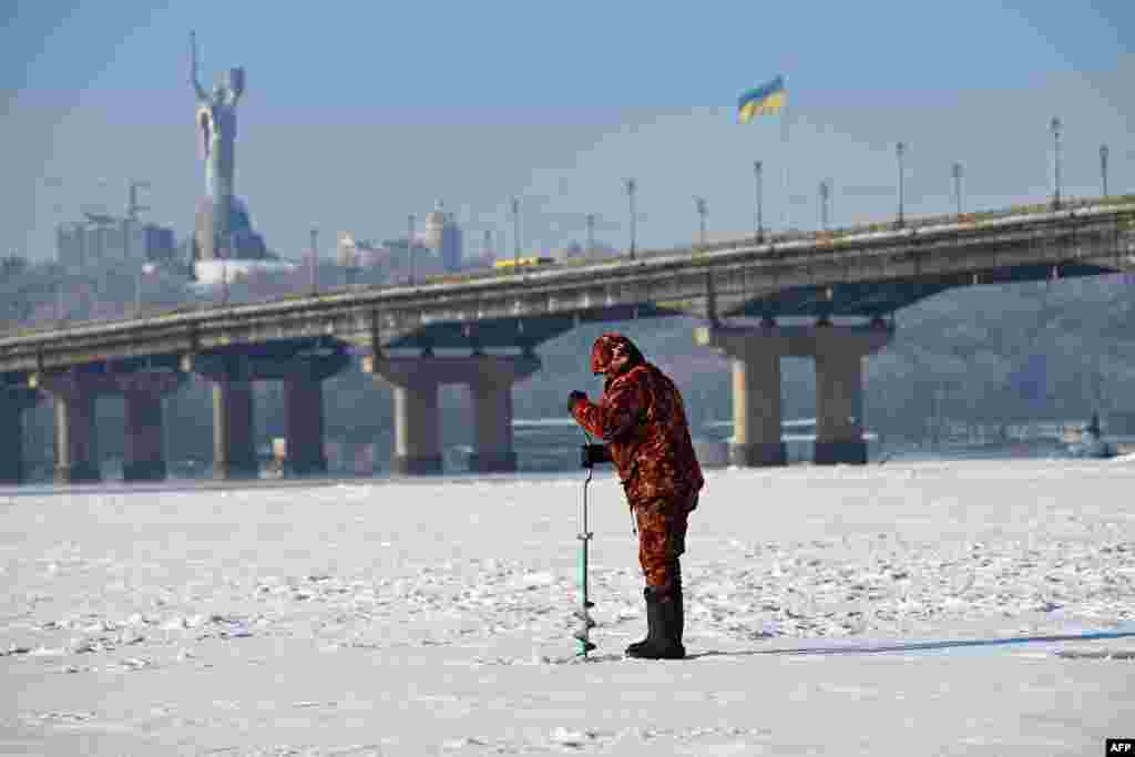 Un pescar pe râul Nipru acoperit de gheață, la Kiev, cu Monumentul Patriei și un steag ucrainean gigant în fundal, pe 16 ianuarie.
