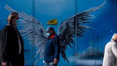 Persona me maskë mbrojtëse kalojnë pranë një murali në një qendrë tregtare në Berlin të Gjermanisë. 