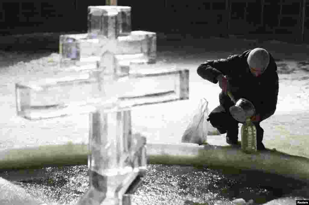 A man bottles holy water from a pool under an Orthodox cross made of ice during a ceremony to celebrate Epiphany in Tyumen, Russia. (Reuters/Eduard Korniyenko)