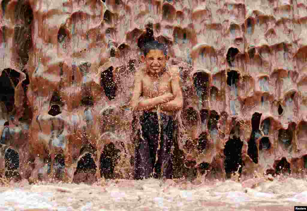 An Afghan boy cools off under a muddy waterfall on the outskirts of Jalalabad Province. (Reuters/Parwiz)