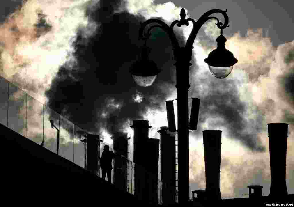 A man poses for a picture on a pedestrian bridge at the Zaryadye Park, with a power plant in the background, in downtown Moscow. (AFP/Yury Kadobnov)