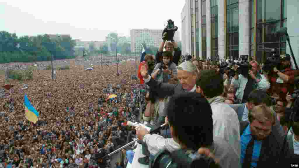 Виступ президента РРФСР Бориса Єльцина на мітингу в Москві, 20 серпня, 1991 року. На мітингу майорять і українські прапори, на передньому плані &ndash; синьо-жовтий прапор, а на задньому &ndash; червоно-чорний. Українці брали активну участь в масових акціях у Москві, які, в кінцевому результаті, призвели до розпаду радянської імперії. Зокрема, із 1989 року в Москві діяла організація з назвою &laquo;ОУН-РУХ&raquo;