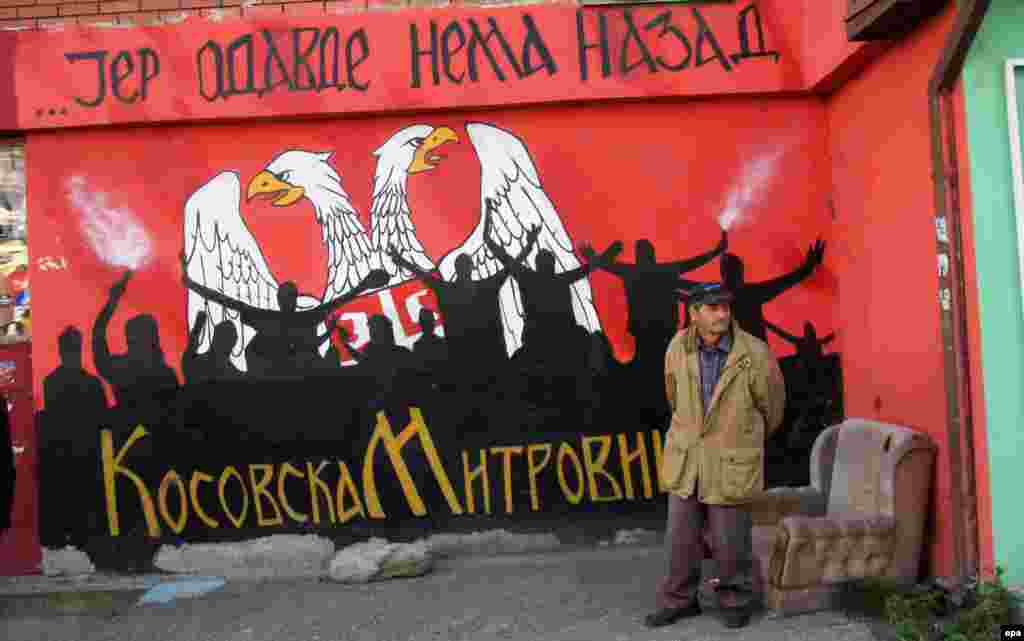An ethnic Serbian man stands next to a mural reading, "Stay here, there is no step back," during a protest rally in the northern part of the ethnically divided town of Mitrovica, in Kosovo. (epa/Djordje Savic)