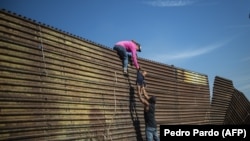 Мигранты перебираются через пограничную ограду в районе мексиканского города Педро Пардо.